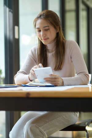 Portrait of a beautiful Asian young woman calculate her monthly expenses and plan her investment strategy.の写真素材