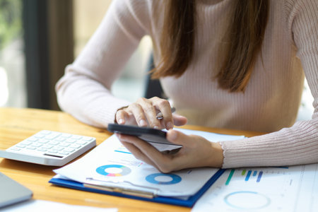 Close-up shot, A female financial worker using mobile phone, searching some details on smartphone over her office desk.の写真素材