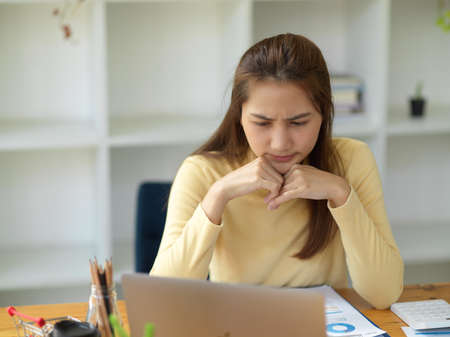 A stressed-out businesswoman is working, focused on her laptop screen, analyzing data and pondering the best way to solve problems.の写真素材