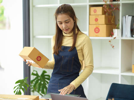A female entrepreneur holding a small parcel box and checking the purchase order on tablet computer. SME, small business, e-commerce business conceptの写真素材