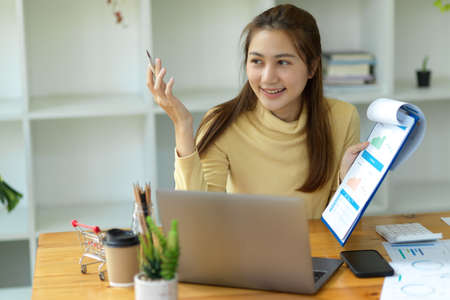 A female businesswoman is talking and showing the report to her colleagues on online meeting via laptop computer in the office.の写真素材