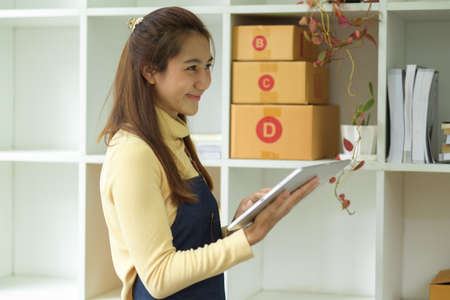 A female small business entrepreneur checking her product details on digital tablet touchpad in her office. SME, e-commerceの写真素材