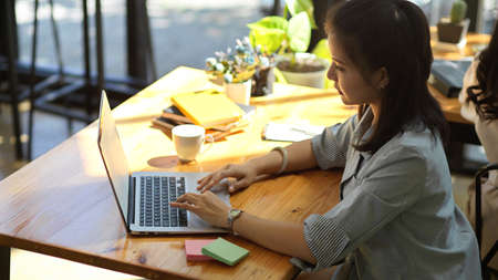Side view, A professional female manager working, typing on portable laptop keyboard in cafe. Businesswoman and remote work concept.の写真素材