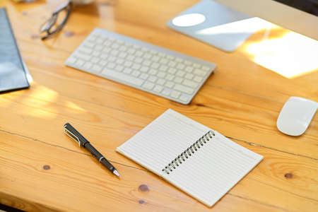 Modern office workspace with office supplies, stationery, wireless keyboard, pc desktop computer, an open empty spiral notepad on wooden table. close-upの写真素材