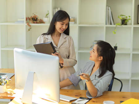 Beautiful Asian young female colleagues are talking and planning their work on pc computer together.の写真素材