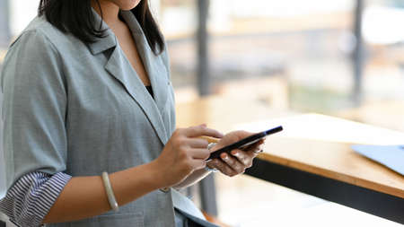 Close-up, A female uses a smartphone at a cafe. A businesswoman in a casual suit contacts her colleague with her smartphone.の写真素材