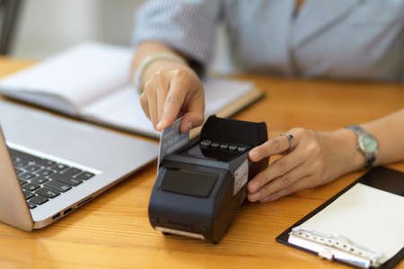 Cropped image, A female cashier swipe a credit card on payment terminal machine on her desk. Cashless payment, electronic wallet.の写真素材