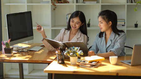 Two cheerful Asian female employee are discussing her project plan and process in their office workplace.の写真素材