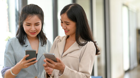 A female sharing some online content on social media to her friend. A young female worker showing her picture to her colleague.の写真素材