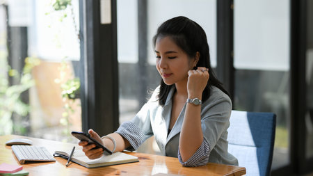Attractive asian female executive manager using her phone at her office desk. texting, chatting, browsing internet.の写真素材