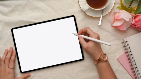 Female office desk with accessories and a female hands drawing on digital tablet touchpad. A mockup of tablet white screen with a female handsの写真素材