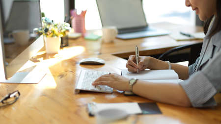 Close-up, A Businesswoman taking notes on notebook and searching some informations on pc computer.の写真素材