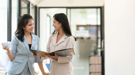 Two attractive and cheerful asian businesswomen having a relax conversation in the office hallway. teamwork business people.の写真素材
