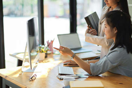 Charming asian businesswoman showing the research result on pc desktop screen to her female manager in the office.の写真素材