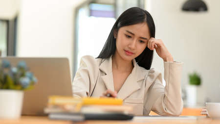 Stressed Asian young businesswoman focusing and concerning about her work project in the office. Female pensive thinking, feeling upset with herself.の写真素材