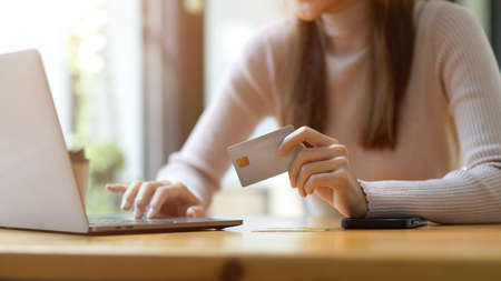 Cropped, close-up image of a young female using laptop computer and holding luxury credit card at her workspace. Online payment, Internet banking, Money transfer.の写真素材