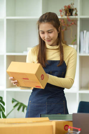 Portrait of a beautiful small business female owner, online seller prepare her delivery package, checks the address details on shipping box in the office.の写真素材