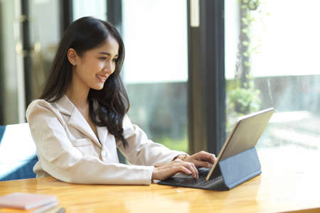 A perfect Asian businesswoman typing on tablet keyboard, working and clearing her assignment.の写真素材