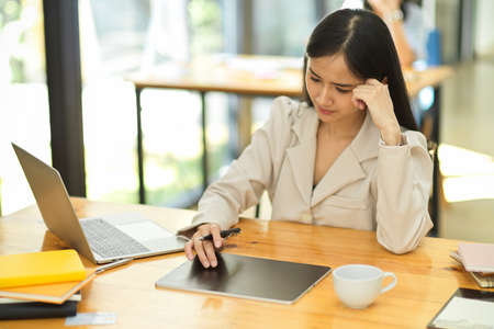 Focused Asian young businesswoman pensive thinking her work project, using digital tablet to search an informations in the office.の写真素材