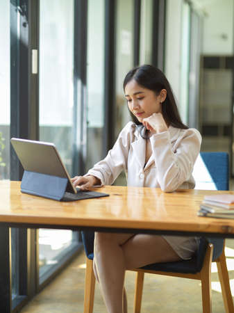 Portrait, Gorgeous Asian young businesswoman or marketing employee remote working in the cafe, working on portable tablet.の写真素材