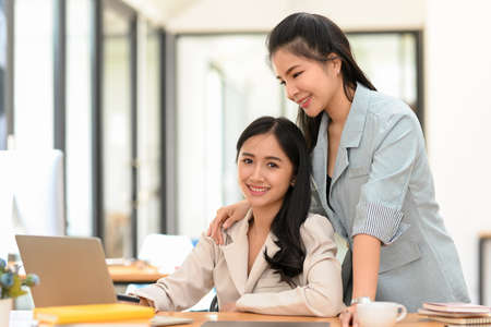 Cheerful business women coworker in modern office, working on project together. Kind female boss training her assistant in the officeの写真素材