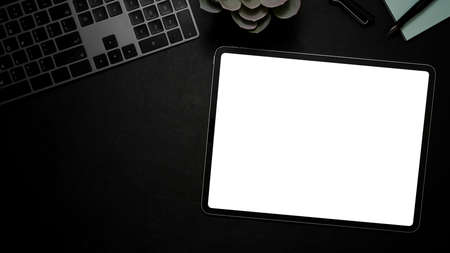 Modern office desk with keyboard, decor plant, tablet white screen mockup and copy space on black...