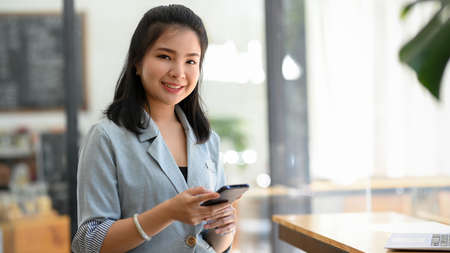 A female in grey casual suit sits in a coffee shop and using her smartphone. People and technology conceptの写真素材