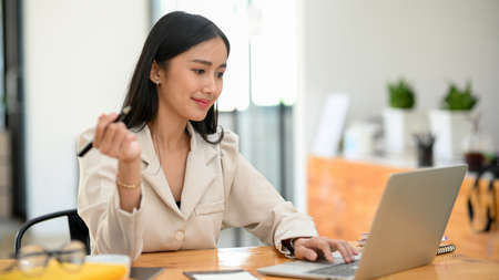 Attractive female boss or business leader working on laptop computer in her modern private office.の写真素材