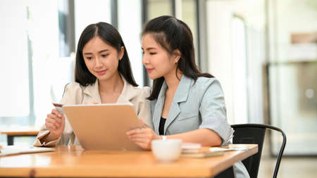 Two female assistant, businesswomen are working together on digital tablet computer. Businesswomen helping, brainstorming their work.の写真素材
