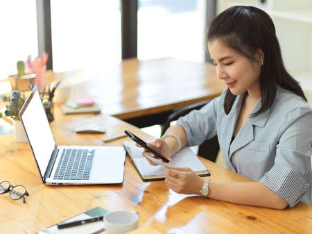 Beautiful asian female typing her credit card password and number to pay her online shopping bills via mobile banking.の写真素材