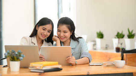 Two female best friends are looking something on digital tablet computer together in the modern office. Happy colleagues working together.の写真素材