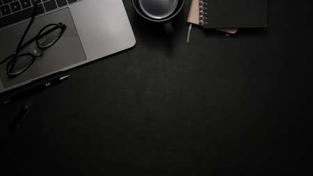Modern office desk with laptop computer, glasses, coffee cup, notebook and copy space on black background. top viewの写真素材