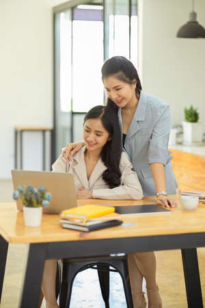 Portrait, Kind and friendly female boss helping and training her young female assistant to work on the hard project. Businesswomen, colleaguesの写真素材