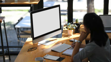 A female assistant or secretary working on her pc desktop computer at her desk. computer white screen mockup.の写真素材