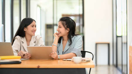 Two happy and charming Asian women relaxes on tablet and enjoy talking in a coffee shop together.の写真素材