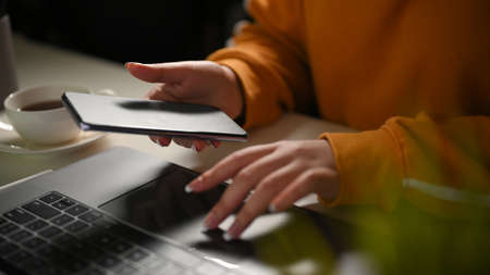 Close-up, A female looking some informations on smartphone screen and typing on laptop keyboard.