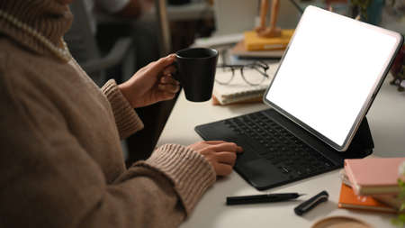 Female freelancer, freelance writer sipping hot coffee while working on her portable tablet computer in her home office. Remote work conceptの写真素材
