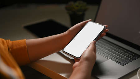 Close-up image, Modern dark workspace with a female hands holding smartphone blank screen mockup over office table.の写真素材