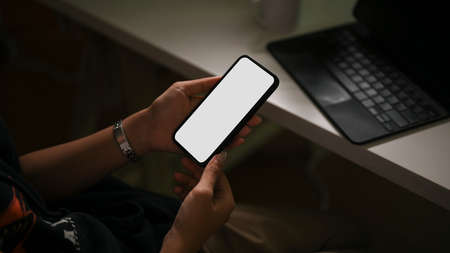 Hipster female using a smartphone in dark office space. Mobile blank screen mockup. close-upの写真素材