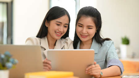 Beautiful asian young female looking interested online content via portable tablet with her college friend.の写真素材