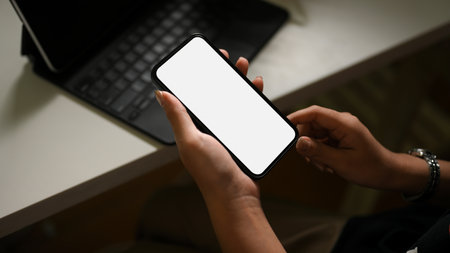 Close-up, focus hands, A female hands holding a smartphone white screen mockup over office desk in dark workspace.の写真素材