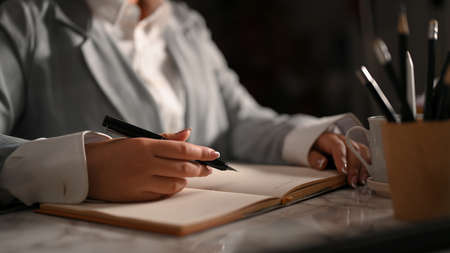 A female executive manager in a formal suit is writing something in her personal notebook and making important notes. in the office.の写真素材