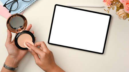 Beauty blogger workspace with digital tablet touchpad white screen mockup, a female hands tapping on...