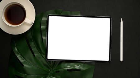 Styled stock photography black office desk table with blank tablet touchpad computer, stylus pen, coffee cup and green leaf. Top view, flat layの写真素材