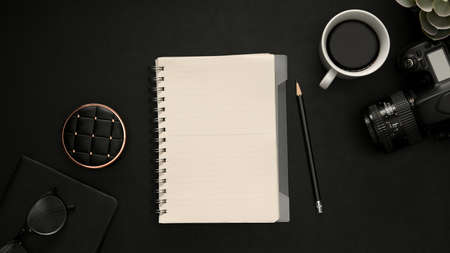 Top view, flat lay, Black workspace background with camera, equipment, coffee cup and empty notebook cover for display your text. Study table, photographer or freelancer workspaceの写真素材
