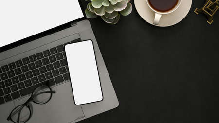 Overhead shot, Modern office desk with laptop computer, glasses, coffee cup, decor plant, smartphone white screen mockup and copy space on black background.の写真素材