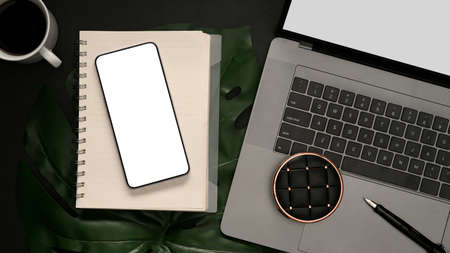 Modern minimal black office desk with laptop computer, smartphone white screen mockup and notebook...