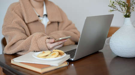 A female college student learning an online class on laptop, An attractive woman remote working at the coffee shop. Female using smartphone and looking at laptop screen.の写真素材