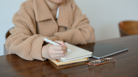 A millennial woman writing down her studying plan in her diary, listing her ideas on spiral notepad, writing notes on notebook, sitting in coffee shop.の写真素材