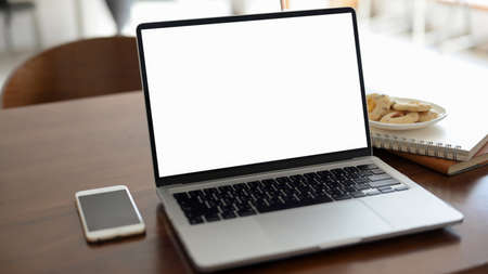 Close-up, A portable laptop computer white screen mockup, smartphone, notebooks, a plate of cookies on wooden office desk. Office desk, study table, remote working cafe's desk.の写真素材